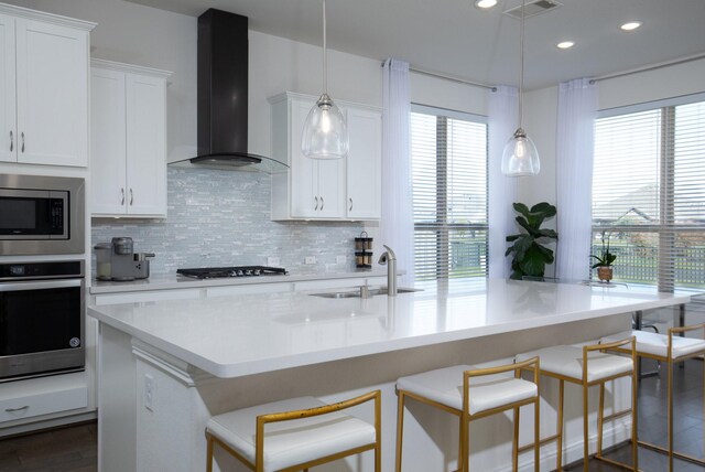 kitchen featuring white cabinetry, a healthy amount of sunlight, wall chimney range hood, and appliances with stainless steel finishes