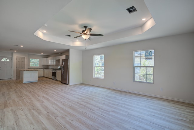 unfurnished living room featuring a raised ceiling, ceiling fan, and light wood-type flooring