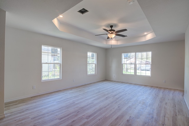 spare room featuring ceiling fan, light hardwood / wood-style floors, a raised ceiling, and a wealth of natural light