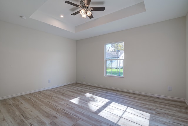 spare room featuring a raised ceiling, light hardwood / wood-style flooring, and ceiling fan