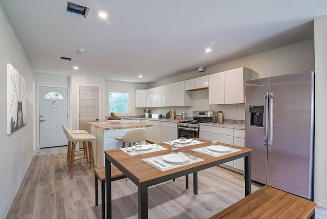 kitchen featuring white cabinets, light hardwood / wood-style floors, a breakfast bar area, a kitchen island, and appliances with stainless steel finishes