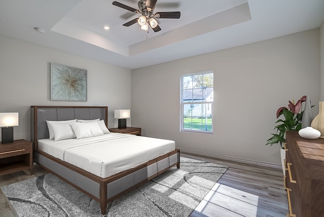 bedroom with hardwood / wood-style flooring, a raised ceiling, and ceiling fan