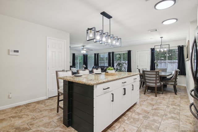 kitchen featuring white cabinets, a center island, decorative light fixtures, and ceiling fan with notable chandelier