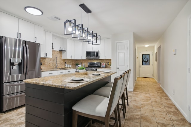 kitchen with white cabinetry, tasteful backsplash, pendant lighting, a kitchen island, and appliances with stainless steel finishes