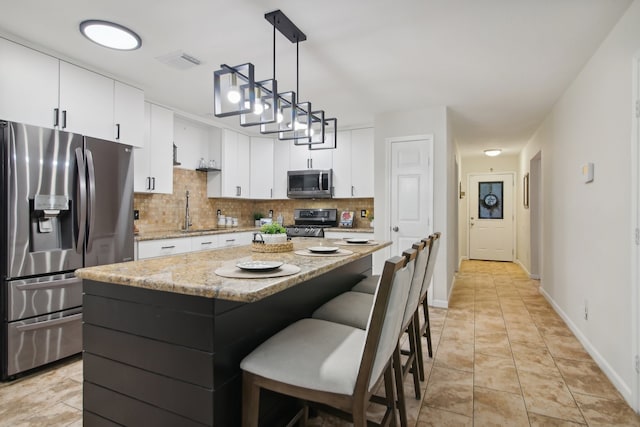 kitchen with white cabinets, hanging light fixtures, tasteful backsplash, a kitchen island, and stainless steel appliances