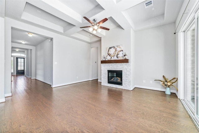 unfurnished living room with ceiling fan, coffered ceiling, a stone fireplace, beamed ceiling, and dark hardwood / wood-style floors