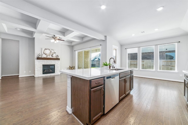 kitchen featuring dark hardwood / wood-style flooring, a kitchen island with sink, sink, dishwasher, and a stone fireplace