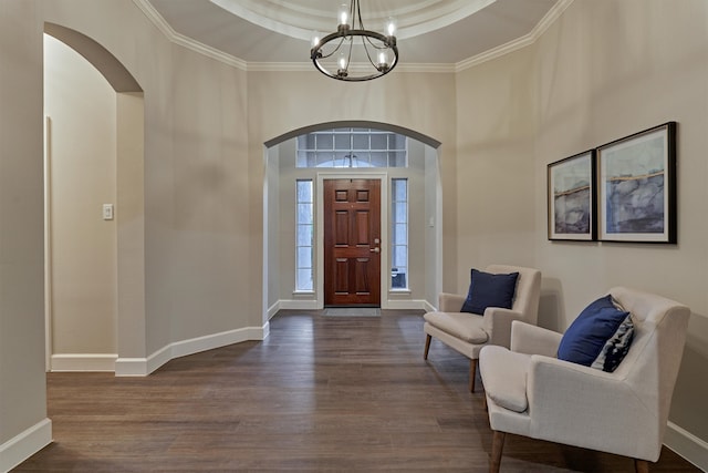 entrance foyer featuring a towering ceiling, a raised ceiling, crown molding, a chandelier, and dark hardwood / wood-style floors