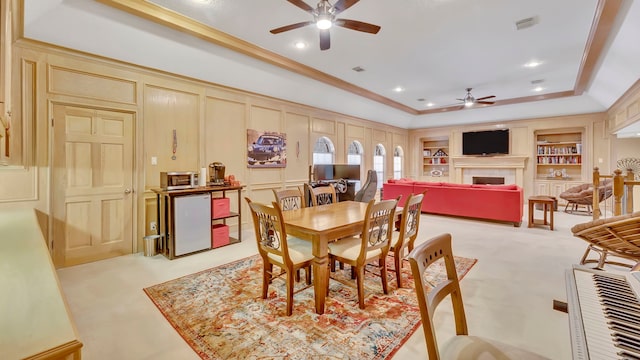 carpeted dining area with ornamental molding, built in features, a raised ceiling, and ceiling fan