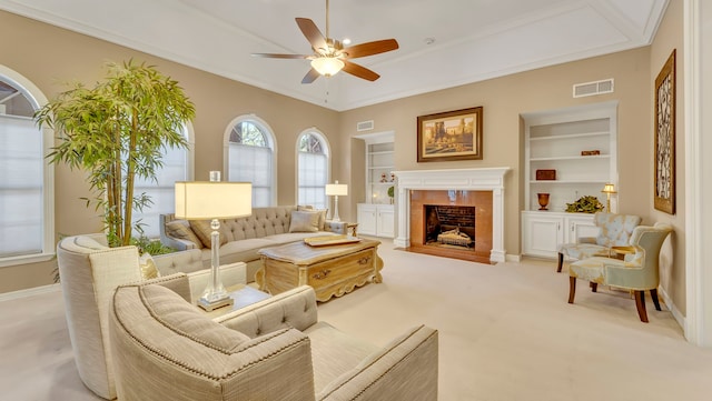 living room with crown molding, ceiling fan, a premium fireplace, light carpet, and built in shelves