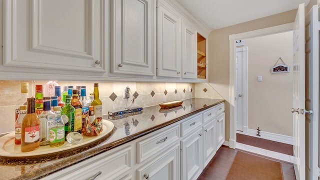 kitchen featuring tasteful backsplash, dark tile patterned floors, white cabinets, and stone counters