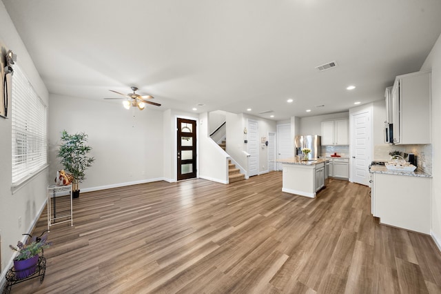 kitchen with a center island with sink, white cabinets, light hardwood / wood-style flooring, tasteful backsplash, and stainless steel appliances