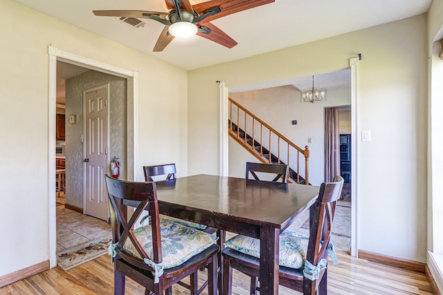 dining space with ceiling fan with notable chandelier and light hardwood / wood-style floors