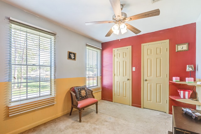 living area featuring light colored carpet, ceiling fan, and a healthy amount of sunlight