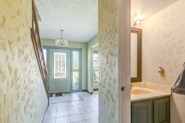 foyer entrance featuring light tile patterned floors, a textured ceiling, an inviting chandelier, and sink