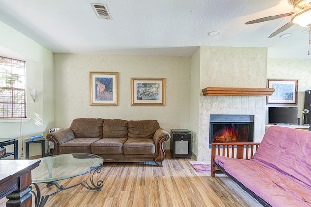 living room with ceiling fan, light hardwood / wood-style floors, a textured ceiling, and a tiled fireplace