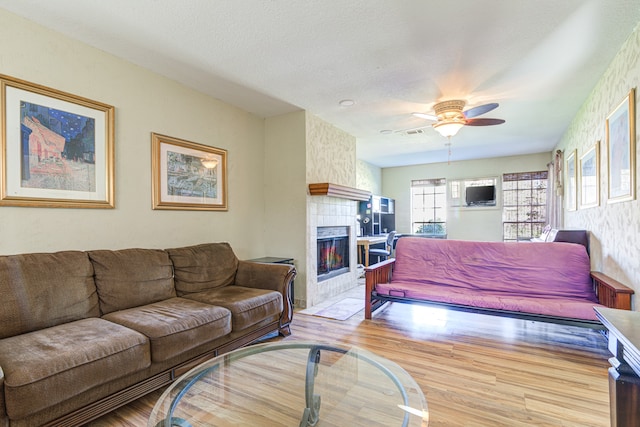 living room with a tiled fireplace, ceiling fan, light hardwood / wood-style flooring, and a textured ceiling