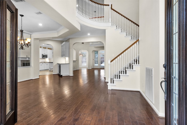 entrance foyer featuring a towering ceiling, an inviting chandelier, dark wood-type flooring, and crown molding