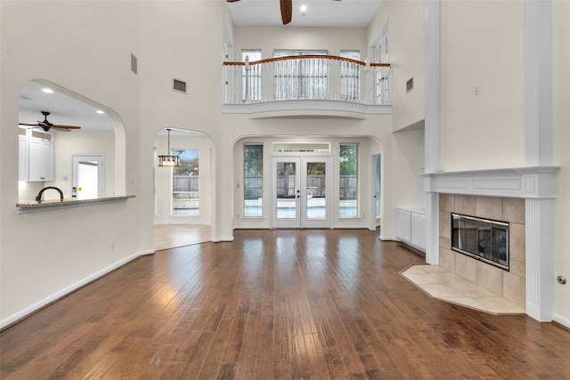 unfurnished living room with french doors, dark hardwood / wood-style floors, ceiling fan, a towering ceiling, and a fireplace