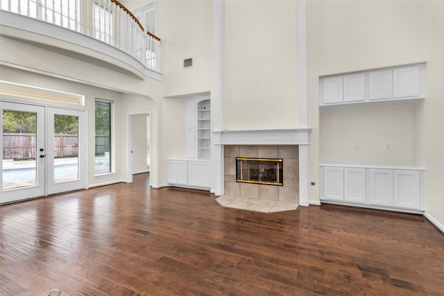 unfurnished living room with a tile fireplace, dark wood-type flooring, a high ceiling, and french doors