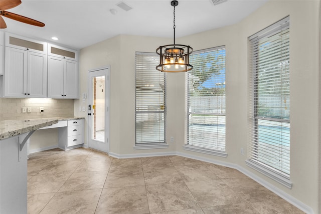 kitchen featuring white cabinets, pendant lighting, light stone counters, and a healthy amount of sunlight