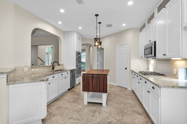 kitchen with light stone countertops, sink, hanging light fixtures, white cabinets, and appliances with stainless steel finishes