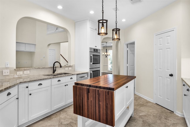 kitchen featuring sink, light stone countertops, appliances with stainless steel finishes, decorative light fixtures, and white cabinetry