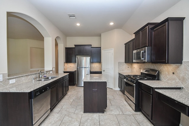 kitchen with appliances with stainless steel finishes, backsplash, sink, light stone counters, and a center island