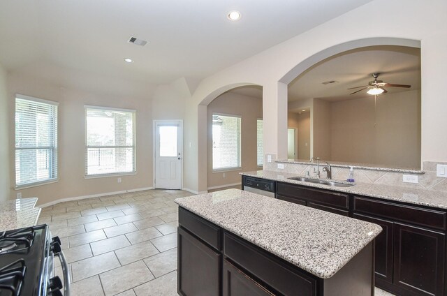 kitchen featuring ceiling fan, gas stove, a kitchen island, sink, and light stone countertops