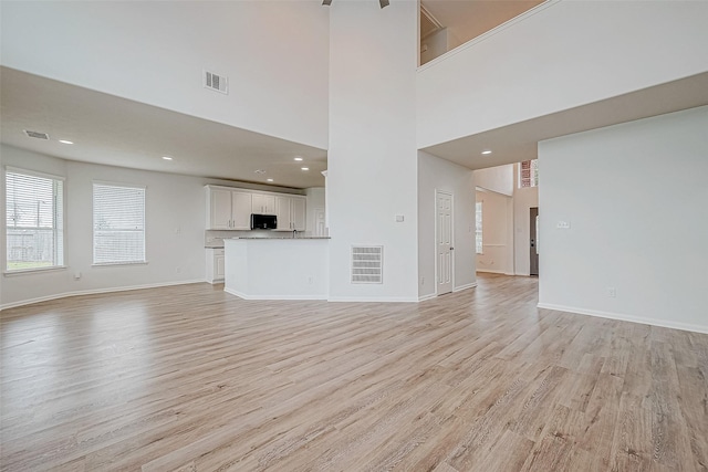 unfurnished living room featuring a high ceiling, light hardwood / wood-style flooring, and ceiling fan