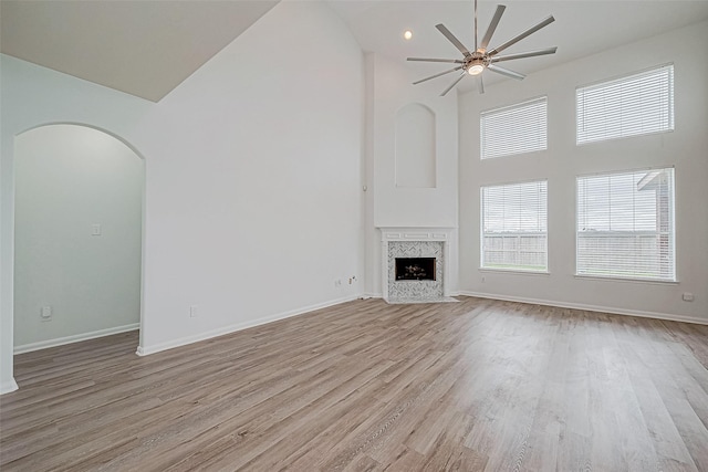 unfurnished living room with ceiling fan, light wood-type flooring, a fireplace, and a high ceiling