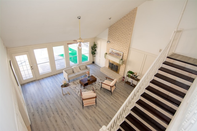 unfurnished living room featuring ceiling fan, light hardwood / wood-style floors, high vaulted ceiling, and a brick fireplace