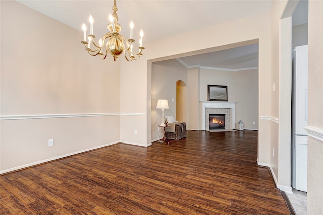 unfurnished living room featuring dark hardwood / wood-style flooring, a tiled fireplace, crown molding, and an inviting chandelier