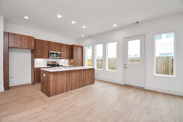 kitchen with appliances with stainless steel finishes, sink, light hardwood / wood-style flooring, and an island with sink