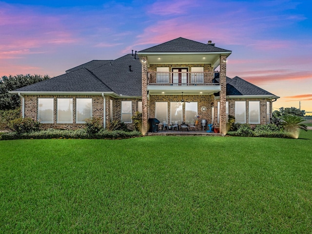 back house at dusk with a balcony and a lawn