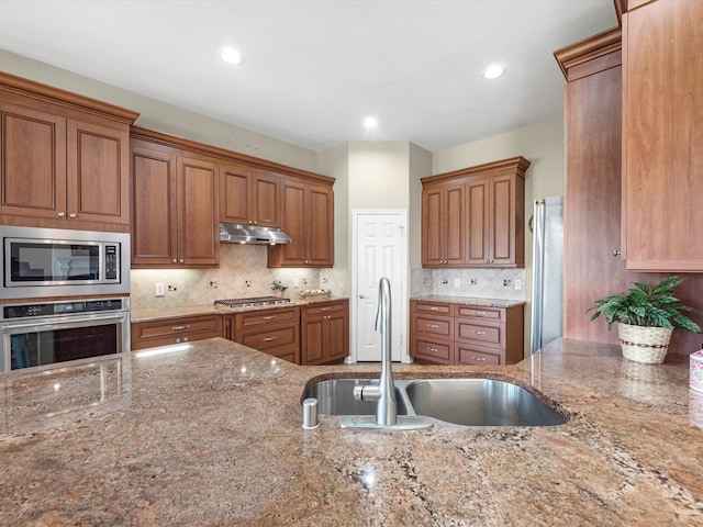 kitchen with appliances with stainless steel finishes, tasteful backsplash, light stone counters, and sink