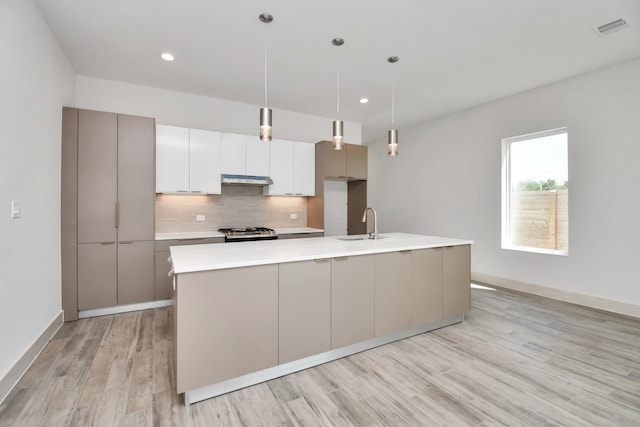 kitchen with decorative backsplash, light wood-type flooring, stainless steel range, a center island with sink, and hanging light fixtures