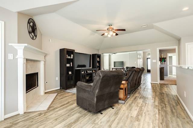 living room with ceiling fan, lofted ceiling, light hardwood / wood-style flooring, and a tiled fireplace