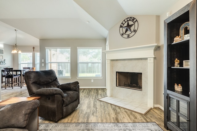 living room featuring hardwood / wood-style flooring, a notable chandelier, lofted ceiling, and a tile fireplace