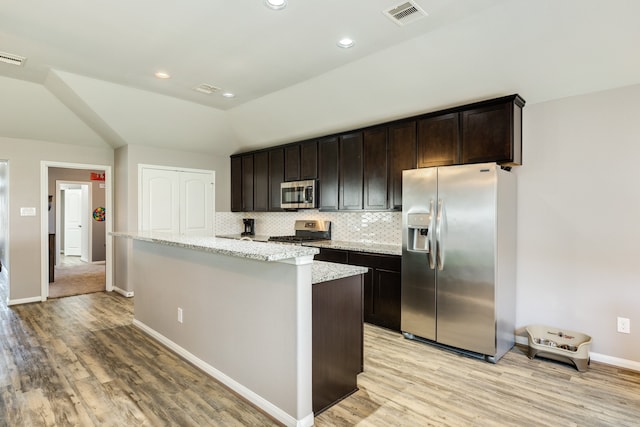 kitchen featuring light stone countertops, appliances with stainless steel finishes, dark brown cabinetry, a center island, and light hardwood / wood-style floors