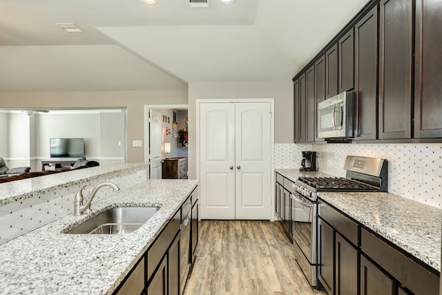 kitchen with light stone countertops, appliances with stainless steel finishes, light hardwood / wood-style floors, and sink