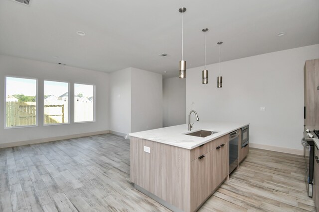 kitchen with sink, light brown cabinets, decorative light fixtures, a kitchen island with sink, and appliances with stainless steel finishes