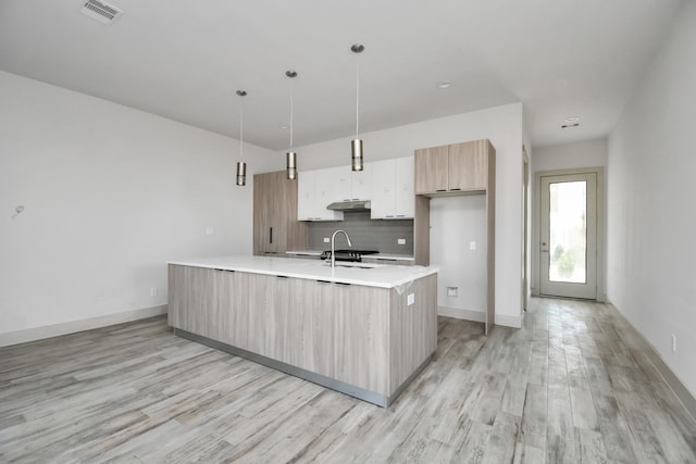 kitchen with sink, tasteful backsplash, light hardwood / wood-style flooring, an island with sink, and pendant lighting