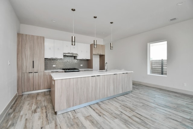 kitchen featuring light wood-type flooring, sink, pendant lighting, a center island with sink, and white cabinets