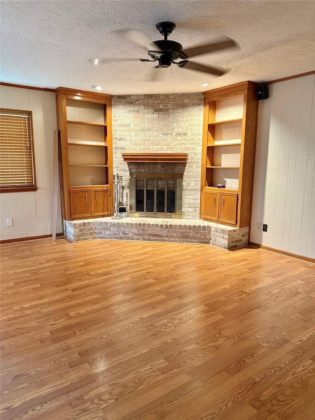 unfurnished living room with built in shelves, a textured ceiling, and a brick fireplace