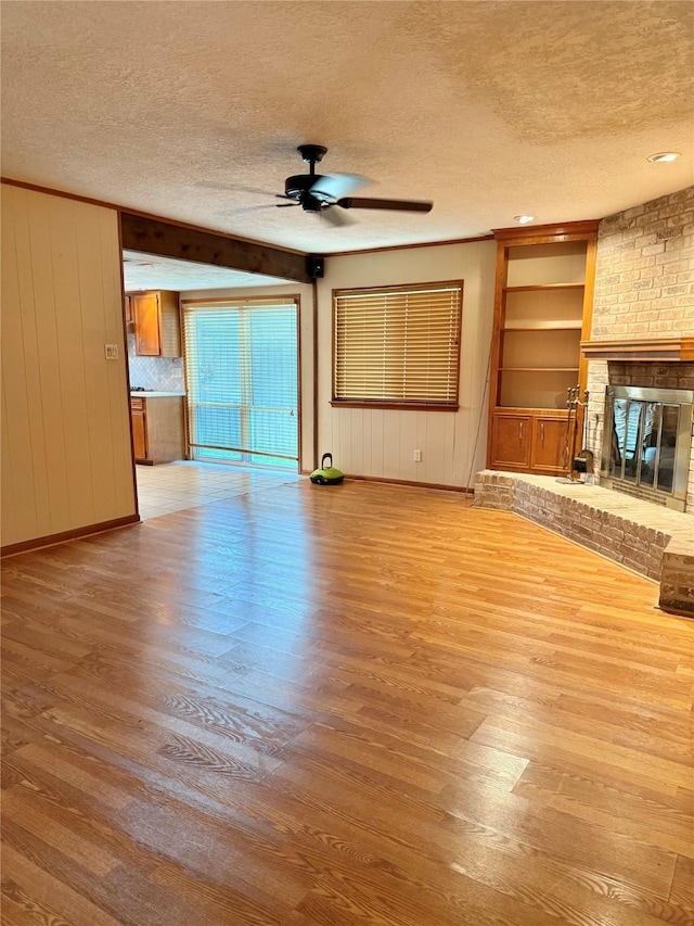 unfurnished living room featuring ceiling fan, a brick fireplace, wood-type flooring, a textured ceiling, and wooden walls