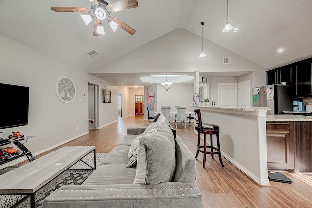 living room with ceiling fan with notable chandelier, light wood-type flooring, and high vaulted ceiling