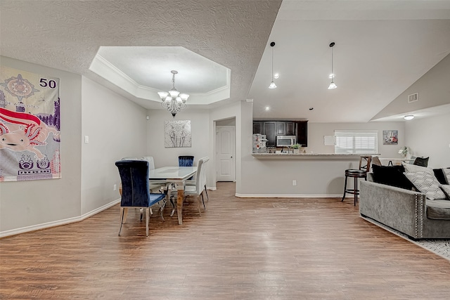 dining room with ornamental molding, a textured ceiling, a raised ceiling, a chandelier, and light hardwood / wood-style floors