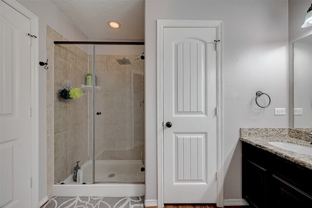 bathroom with vanity, a shower with shower door, and a textured ceiling