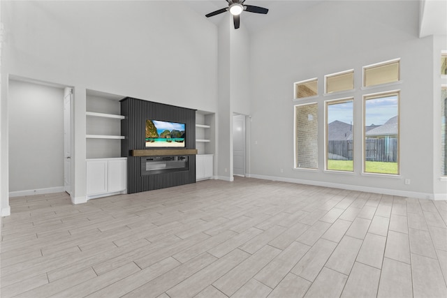 unfurnished living room with built in shelves, light wood-type flooring, ceiling fan, and a high ceiling